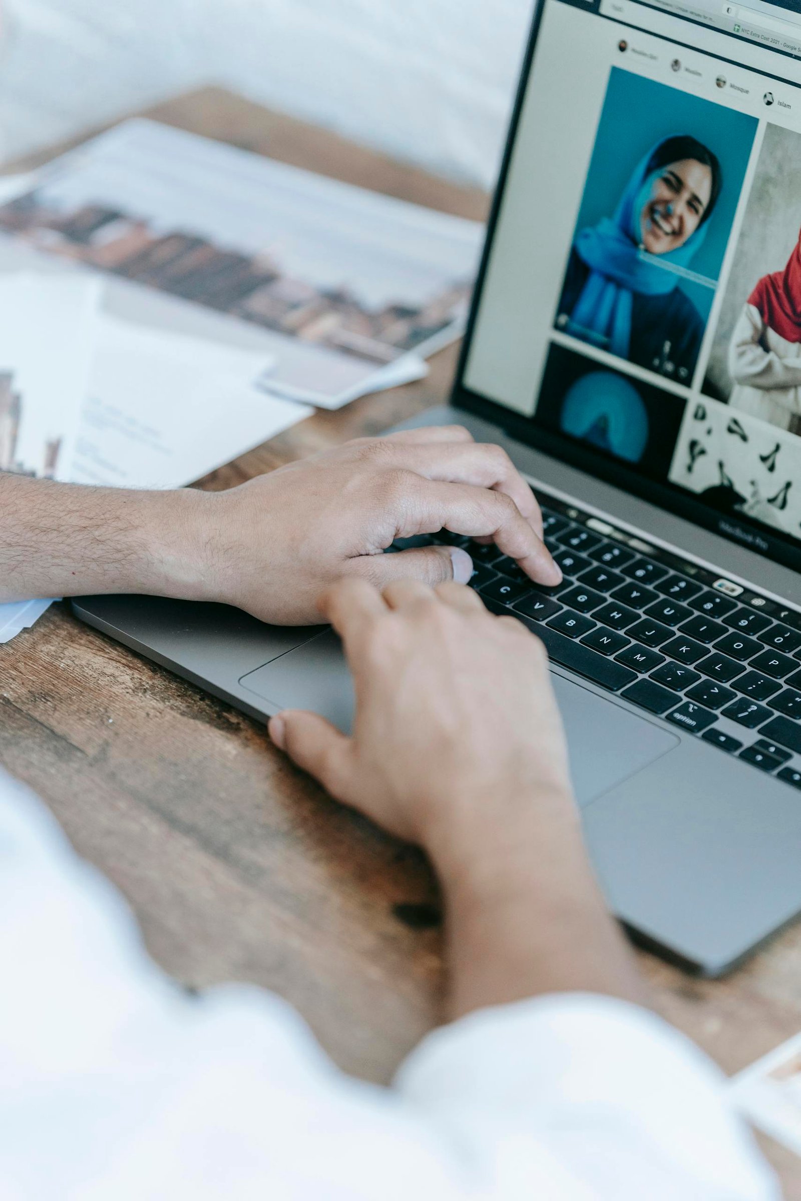 Crop anonymous male photographer creating collage of portrait photos on laptop while working at table in workplace